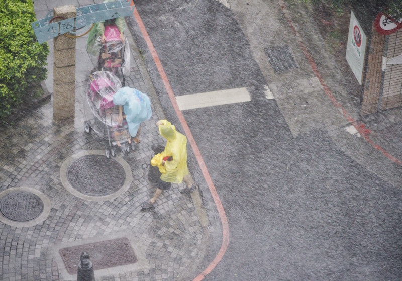 莫蘭蒂颱風襲台，帶來強降雨，帶著小娃兒出門的媽媽，趕快用塑膠雨具遮蔽小孩，免得淋到雨。圖/張良一