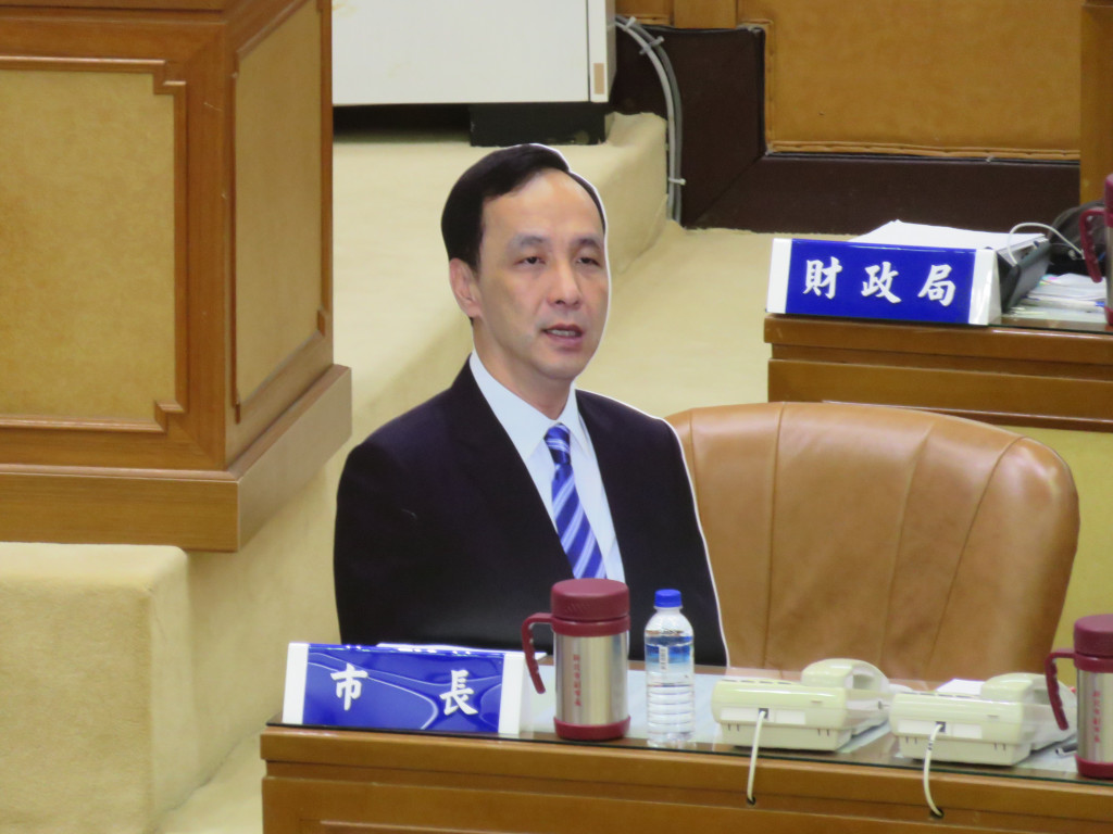 國民黨總統參選人、黨主席兼新北市朱立倫近來四處跑行程，新北市民進黨議會黨團在市長席位上放置朱立倫人形立牌諷刺。（記者唐詩攝影）