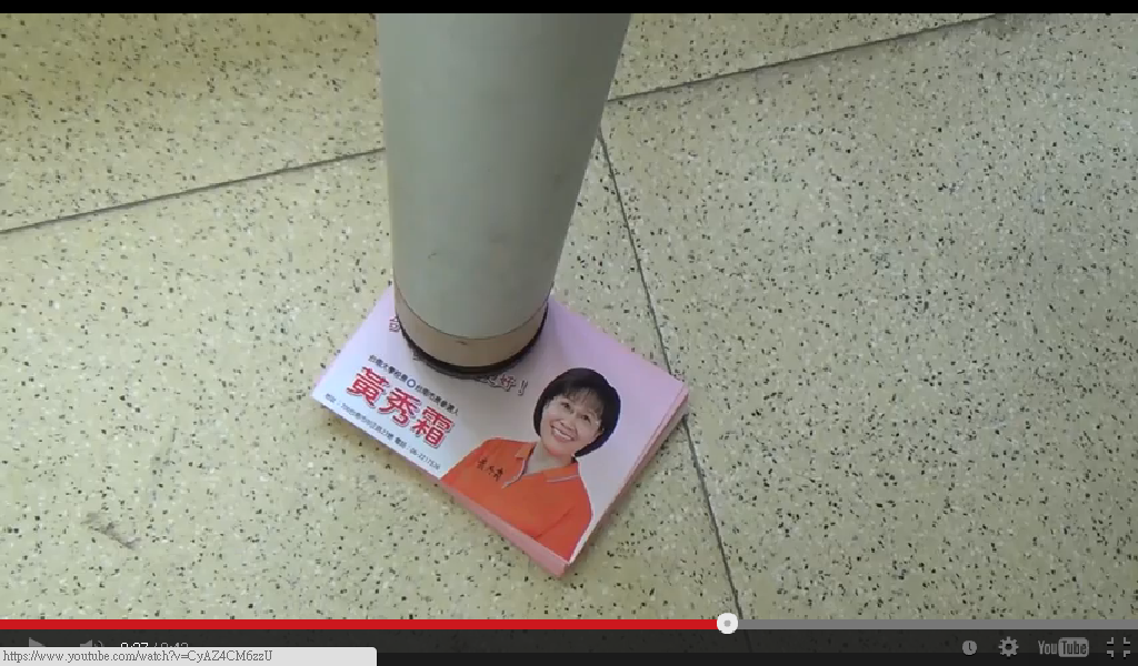 國民黨台南市長提名人黃秀霜新競選影片25日上架，拿著文宣來墊桌腳。（翻攝自網路）