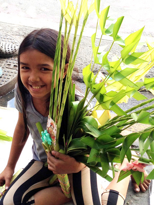 天主教1年1度的聖週29日以「棕枝主日」揭開序幕，菲律賓信徒人手一束棕櫚枝，經教堂神父祝福後帶回家掛在門口趨吉避凶。圖為馬尼拉1名小女孩抱著1束棕枝。（中央社）2015年3月29日